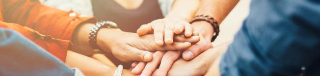 Gruppo eterogeneo di persone con le mani unite, a simboleggiare il lavoro di squadra e la collaborazione.